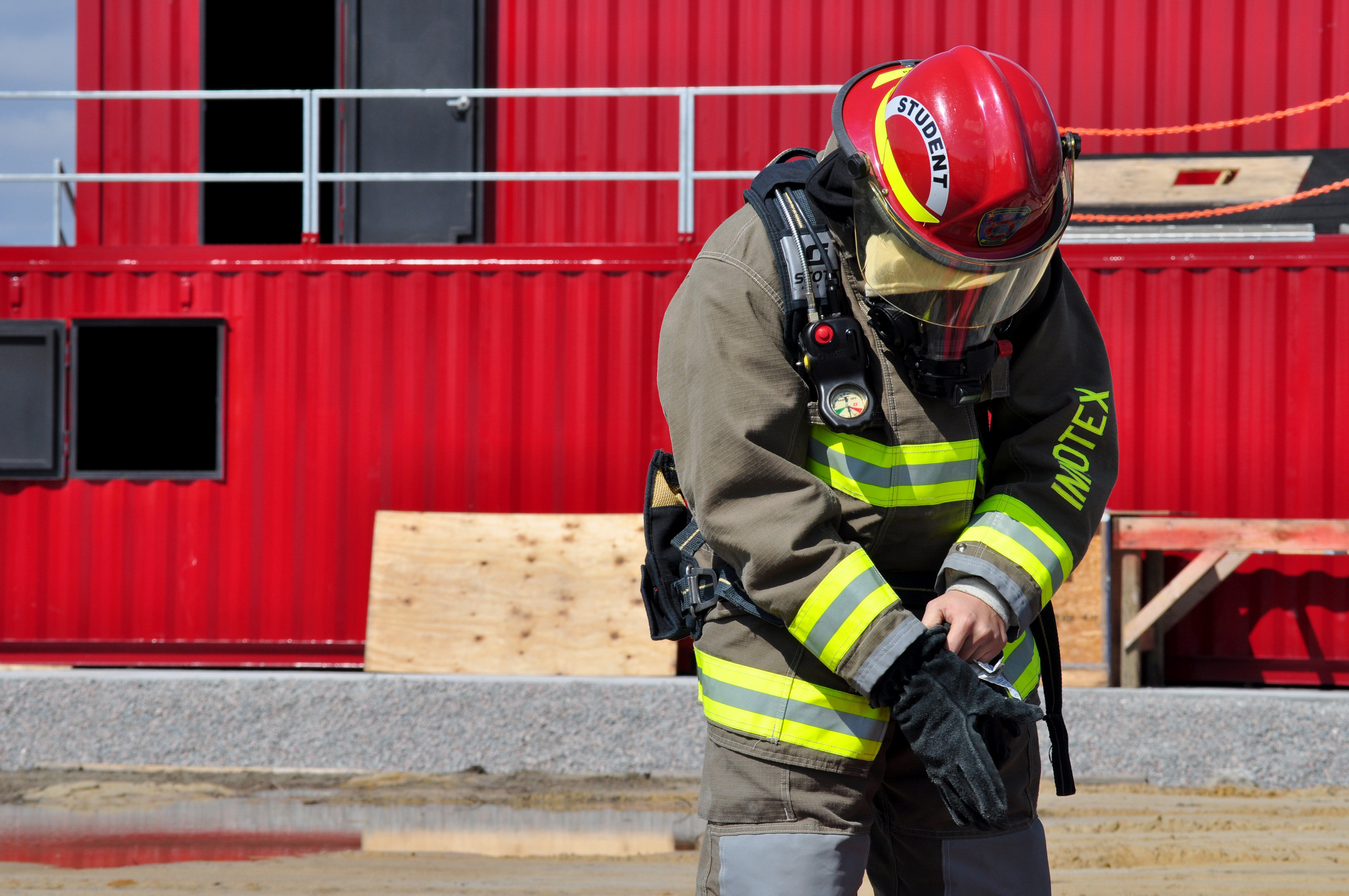 A student firefighter stands in front of a red training area.