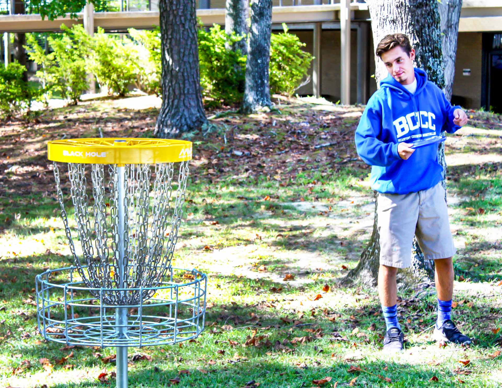A student in a BCCC hoodie with a disc golf basket.